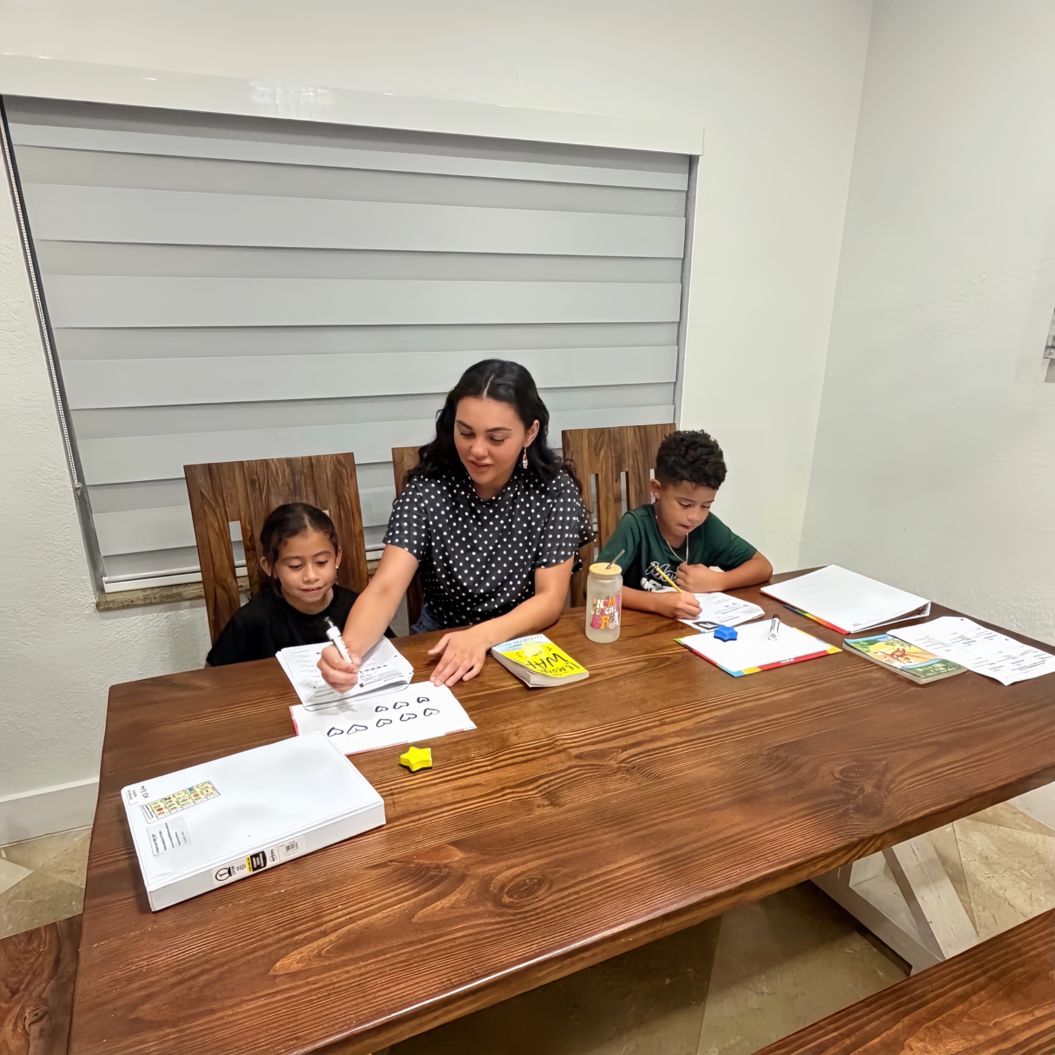 Ms. Liu guiding two students through reading and math practice at a table